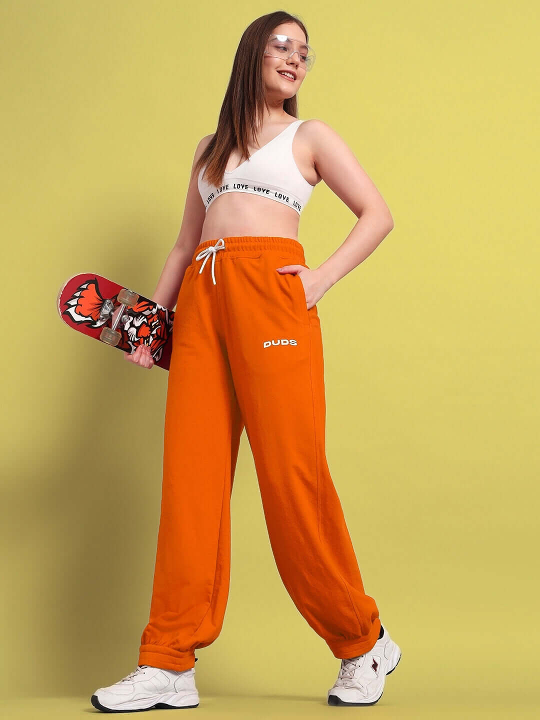 WOMENS AUSTRIAN RELAXED-FIT JOGGERS ORANGE worn by model holding a skateboard in a studio setting