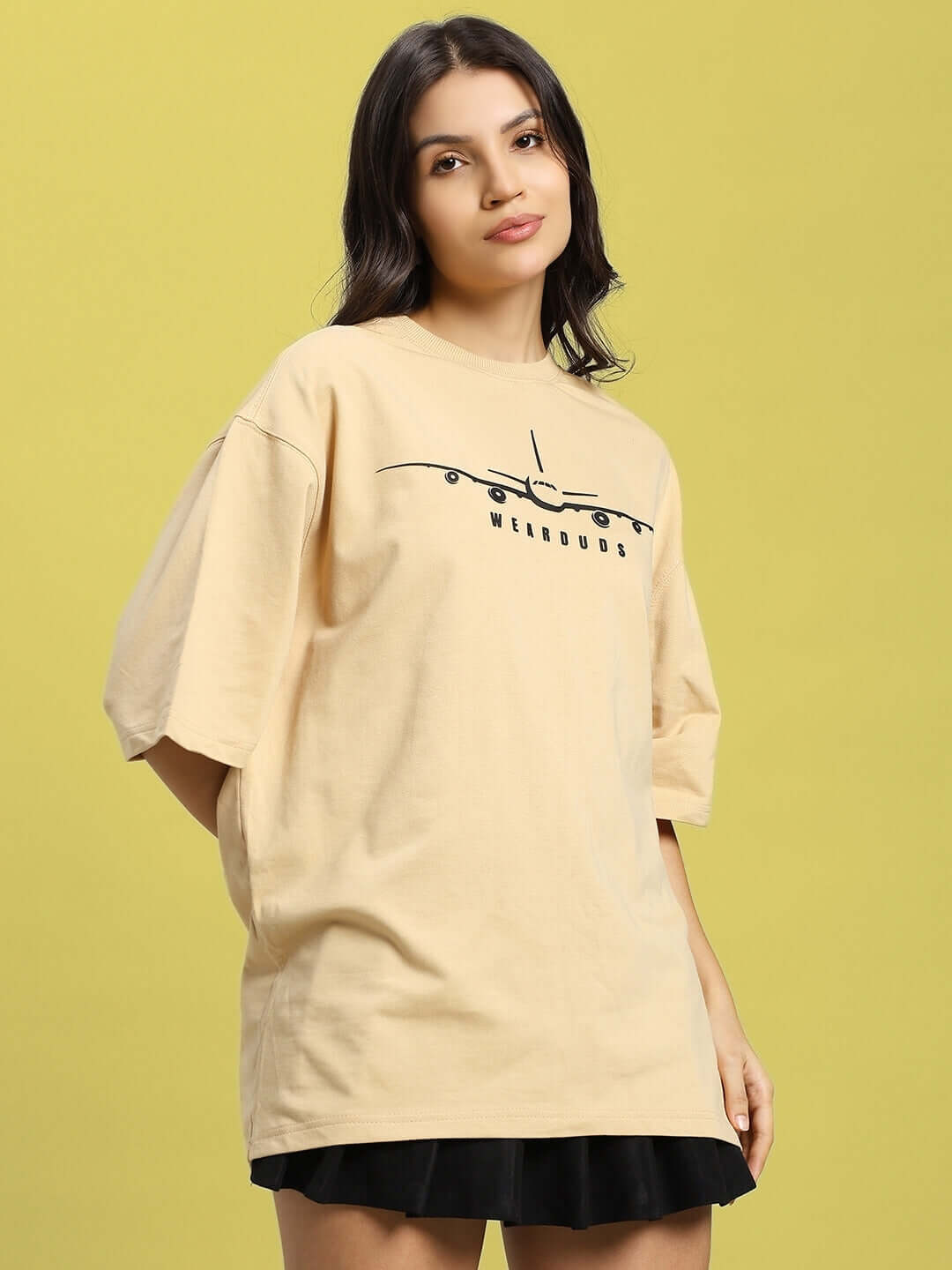 Woman wearing beige oversized women's aviator designer T-shirt made of premium cotton, featuring a stylish design element on the front.