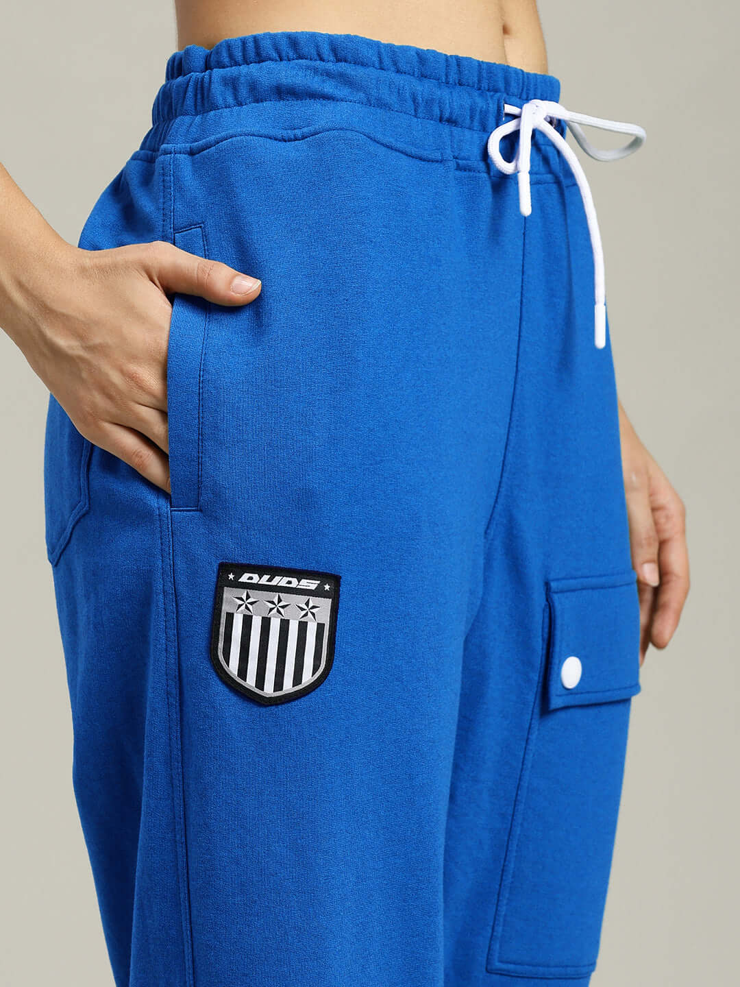 Blue women's baggy jogger with flap pocket and white drawstring, featuring DUDS logo. Perfect for casual wear, customizable fit available.