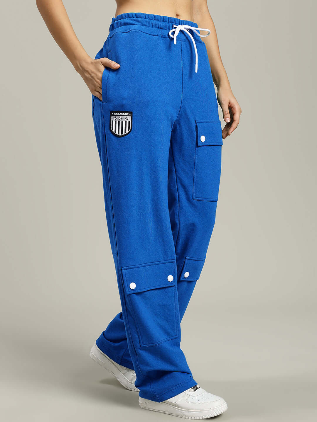Women's blue baggy joggers with flap pockets, elastic waistband, and white drawstrings, worn with white sneakers.