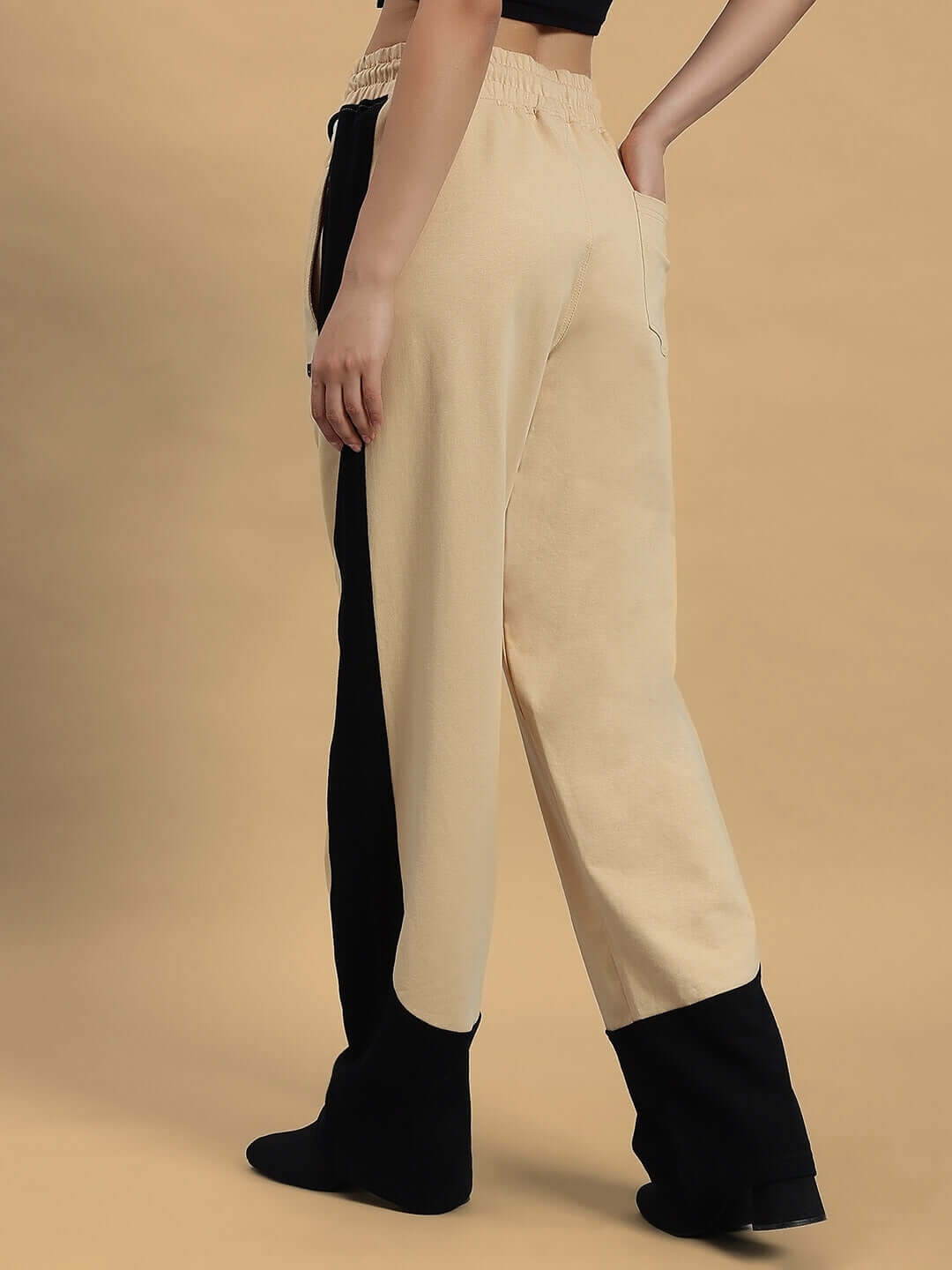 Side view of women's beige-black baggy joggers by DUDS displayed against a beige backdrop, showcasing custom fit option.