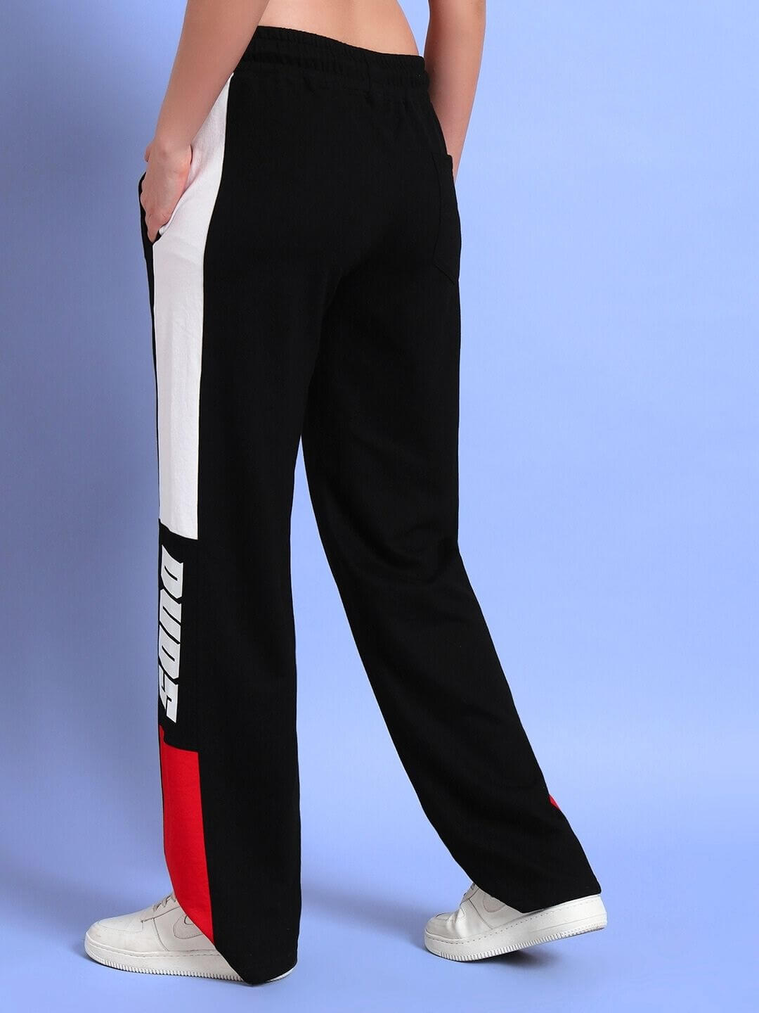 Woman wearing black and red relaxed-fit joggers with "DUDS" logo, standing against a blue background.