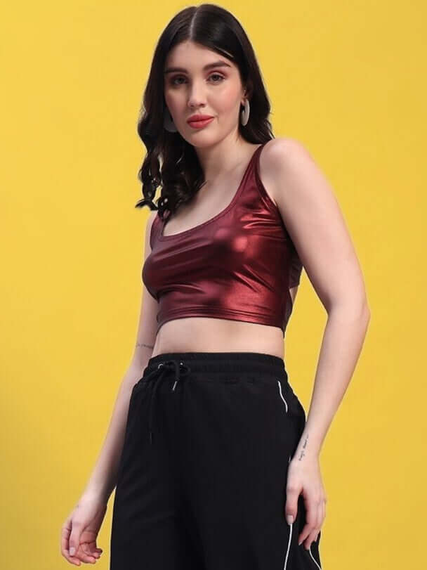 Woman wearing a maroon metallic crop top with black pants, featuring a stylish and contemporary look against a yellow background.