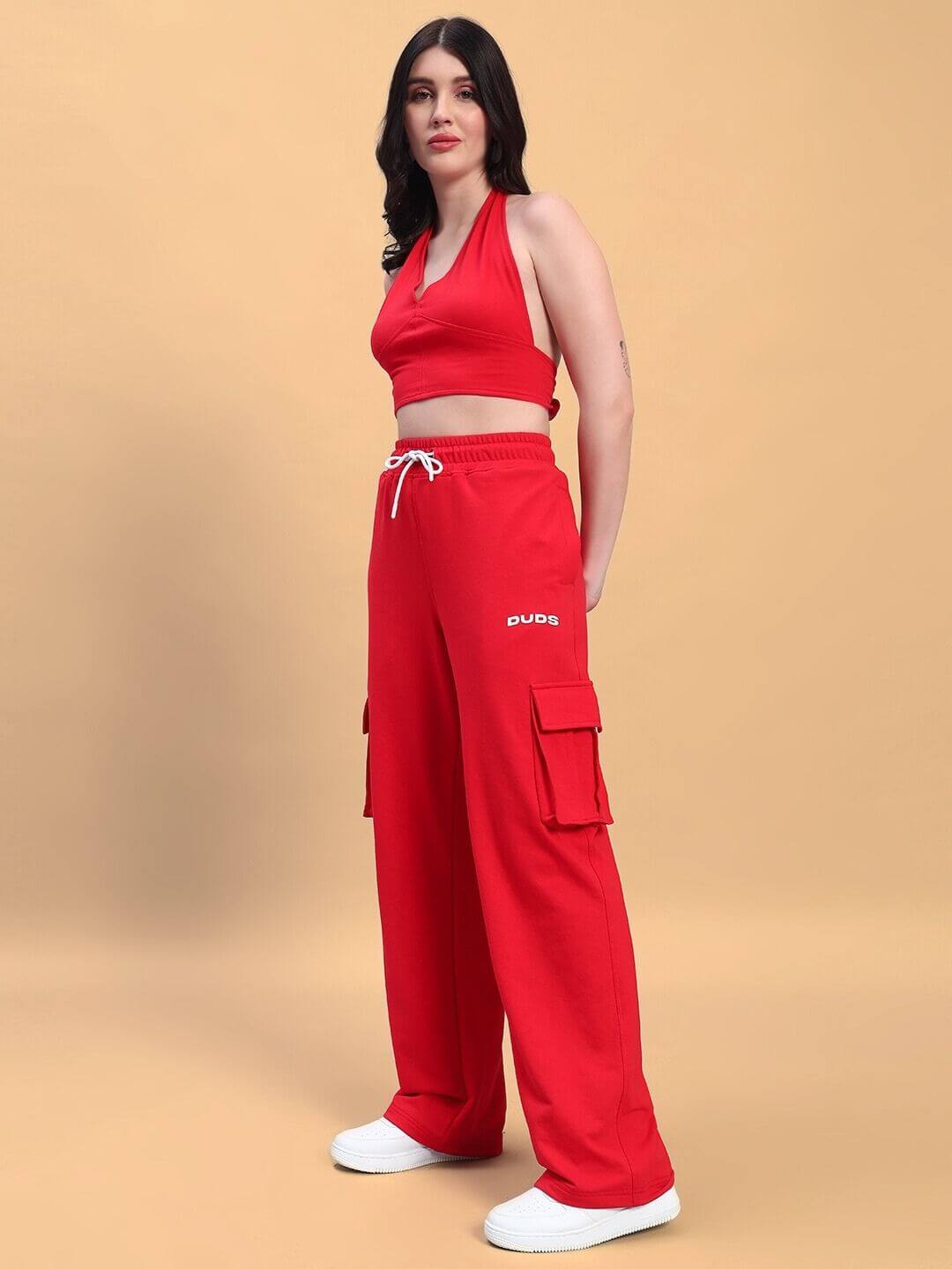 Woman wearing red co-ord set with halter top and cargo pants; premium cotton blend; stands against beige background; stylish fashion.