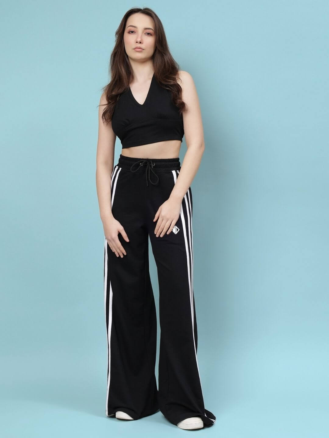 Woman wearing black baggy relaxed-fit jogger with white stripes, styled with a matching sleeveless top against a blue background.