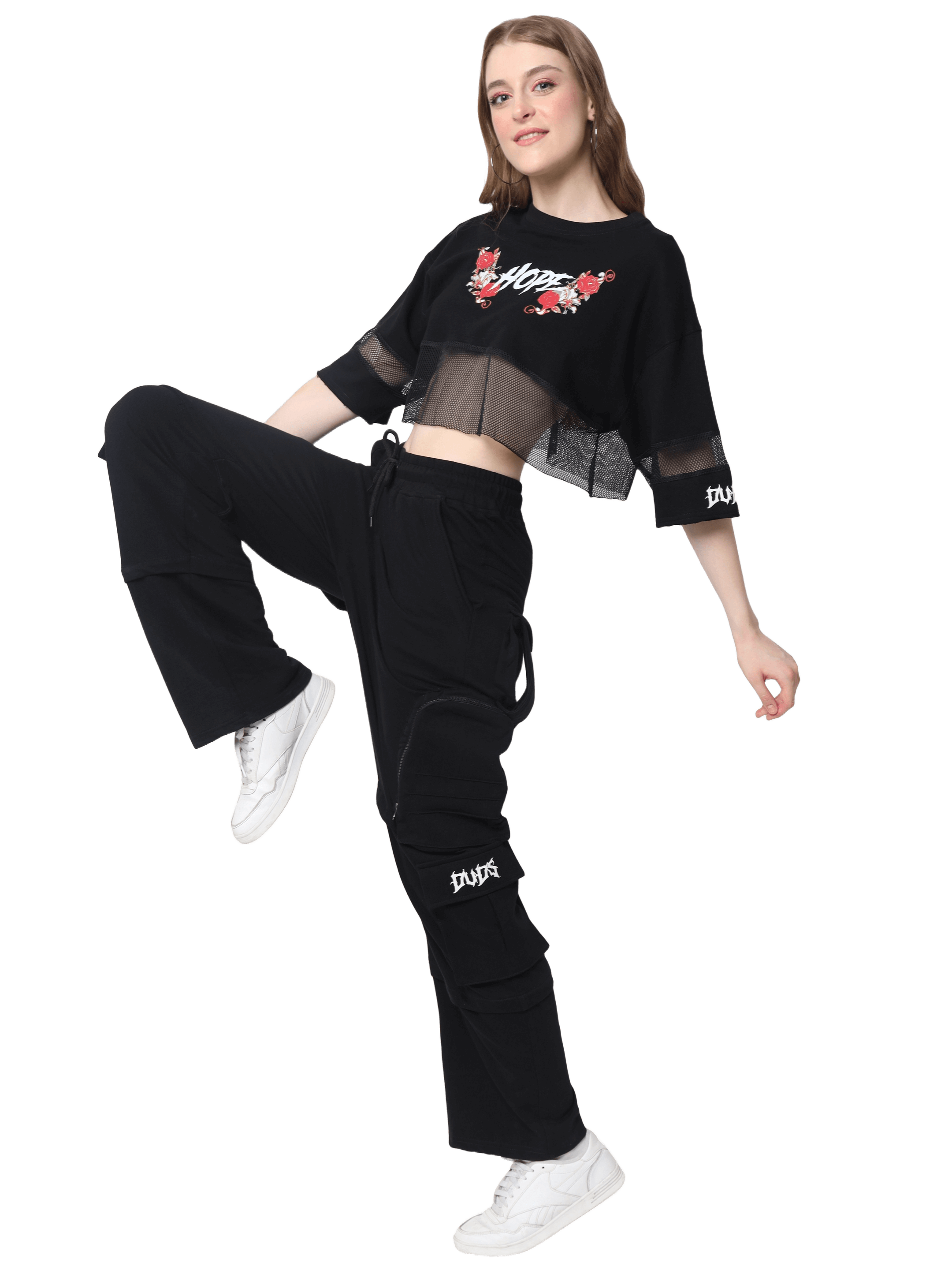 Woman modeling black 8 pocket cargo pants with zipper patch pocket from DUDS, paired with a stylish top and white sneakers.