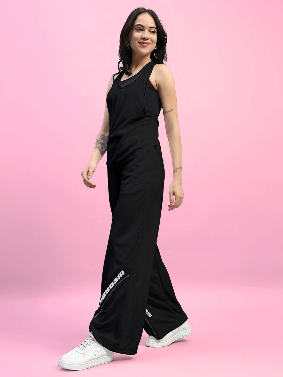 Model wearing Women's Cubby Co-Ord Set in black, featuring relaxed fit joggers and a sleeveless top, on a pink background.