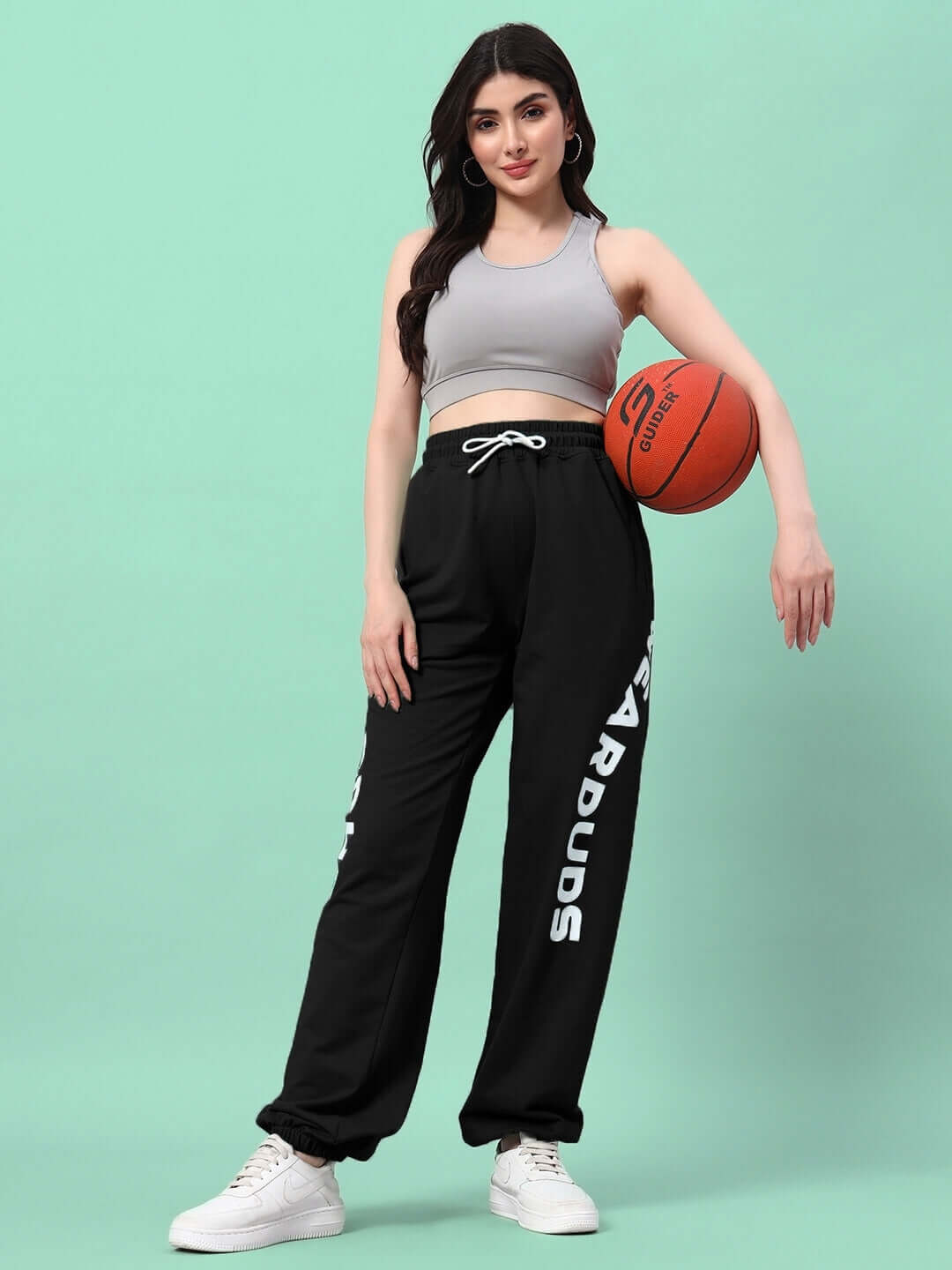 Woman wearing WOMEN'S ELLEN RELAXED FIT JOGGER BLACK holding basketball against mint green background.