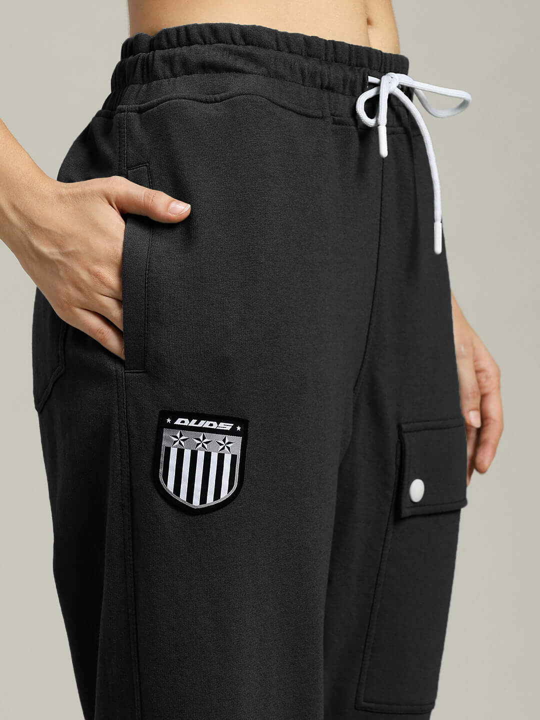 Close-up of black women's jogger pants with flap pocket, showcasing DUDS patch and white drawstring.