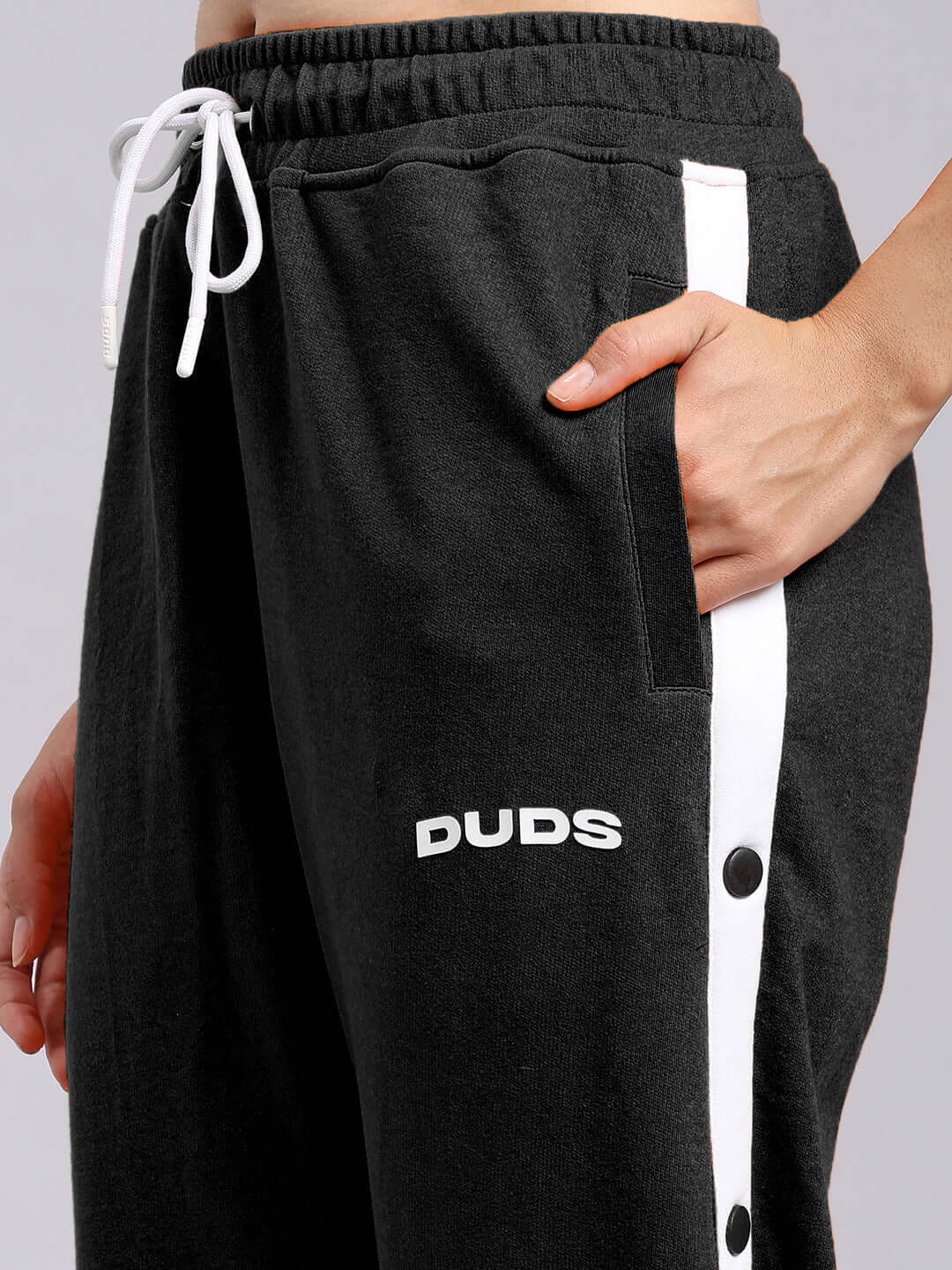 Close-up of black women's relaxed fit joggers with DUDS branding and white side stripe, featuring drawstring and pocket details.