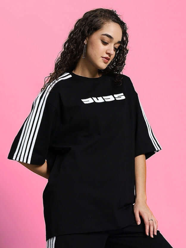 Woman wearing oversized black classic t-shirt with striped sleeves, styled against a pink background.