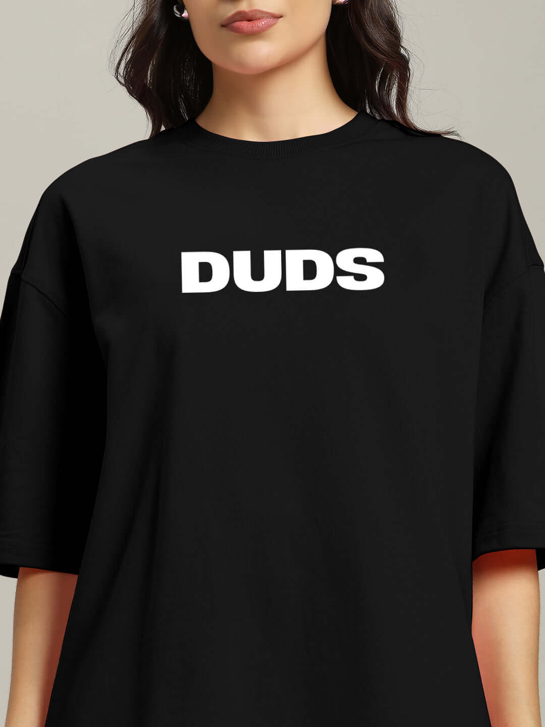 Woman wearing a black oversized T-shirt with 'DUDS' in white text, featuring premium cotton fabric and relaxed fit for casual style.
