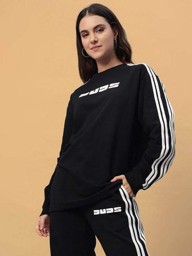 Woman wearing black oversized sweatshirt with sporty design and white stripes on the sleeves, paired with matching track pants.