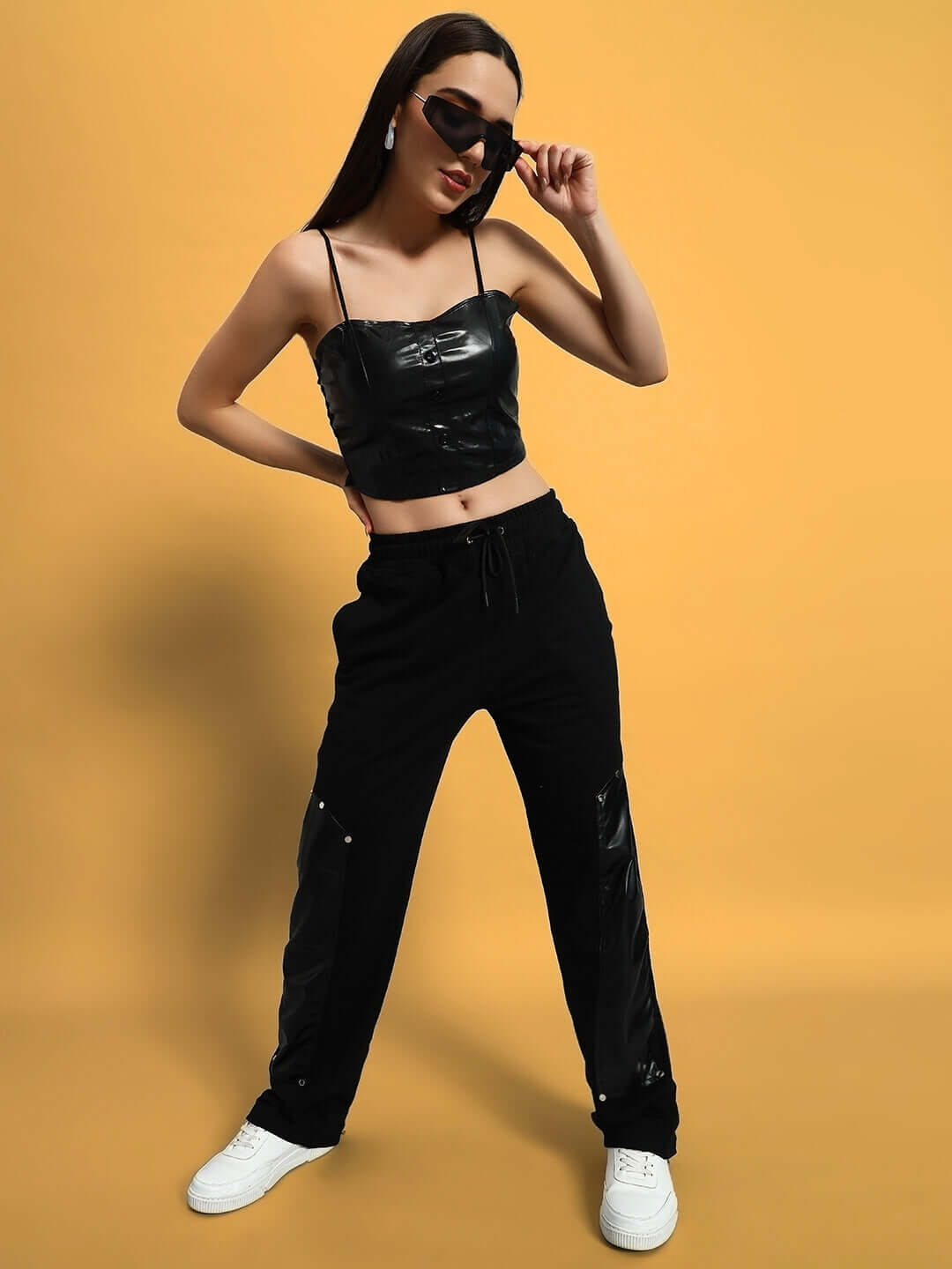 Woman wearing black raccoon leather patch joggers with matching top, styled fashionably with sunglasses against a yellow background.