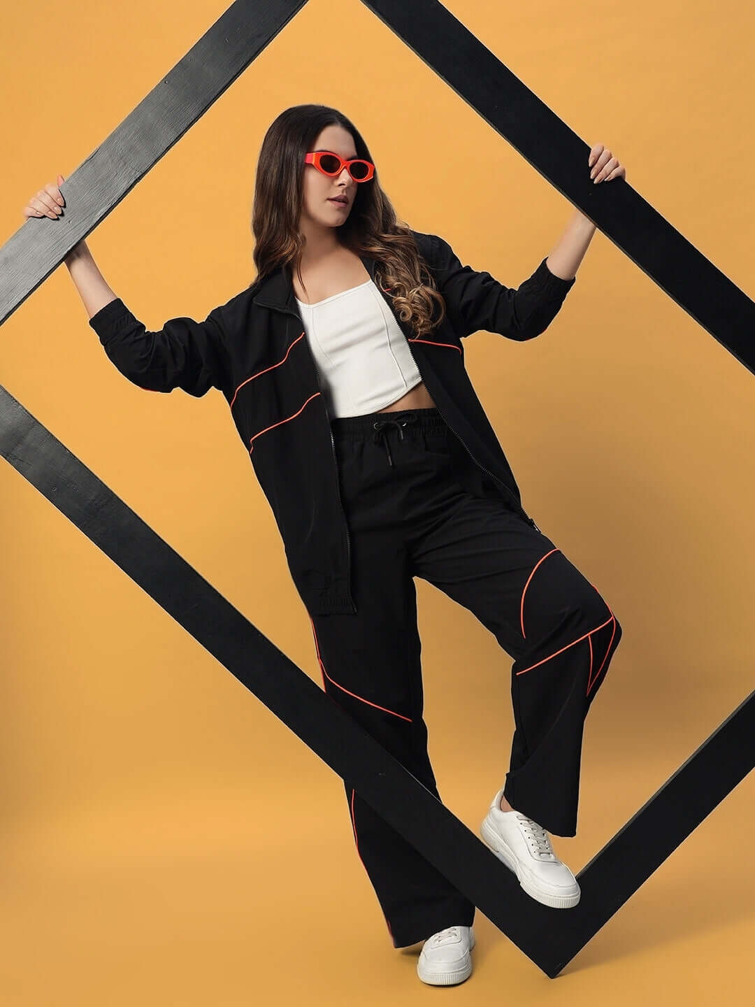Model wearing Women's Raider Co-Ord Set in black with red details, polyester fabric, styled with sunglasses and white sneakers.
