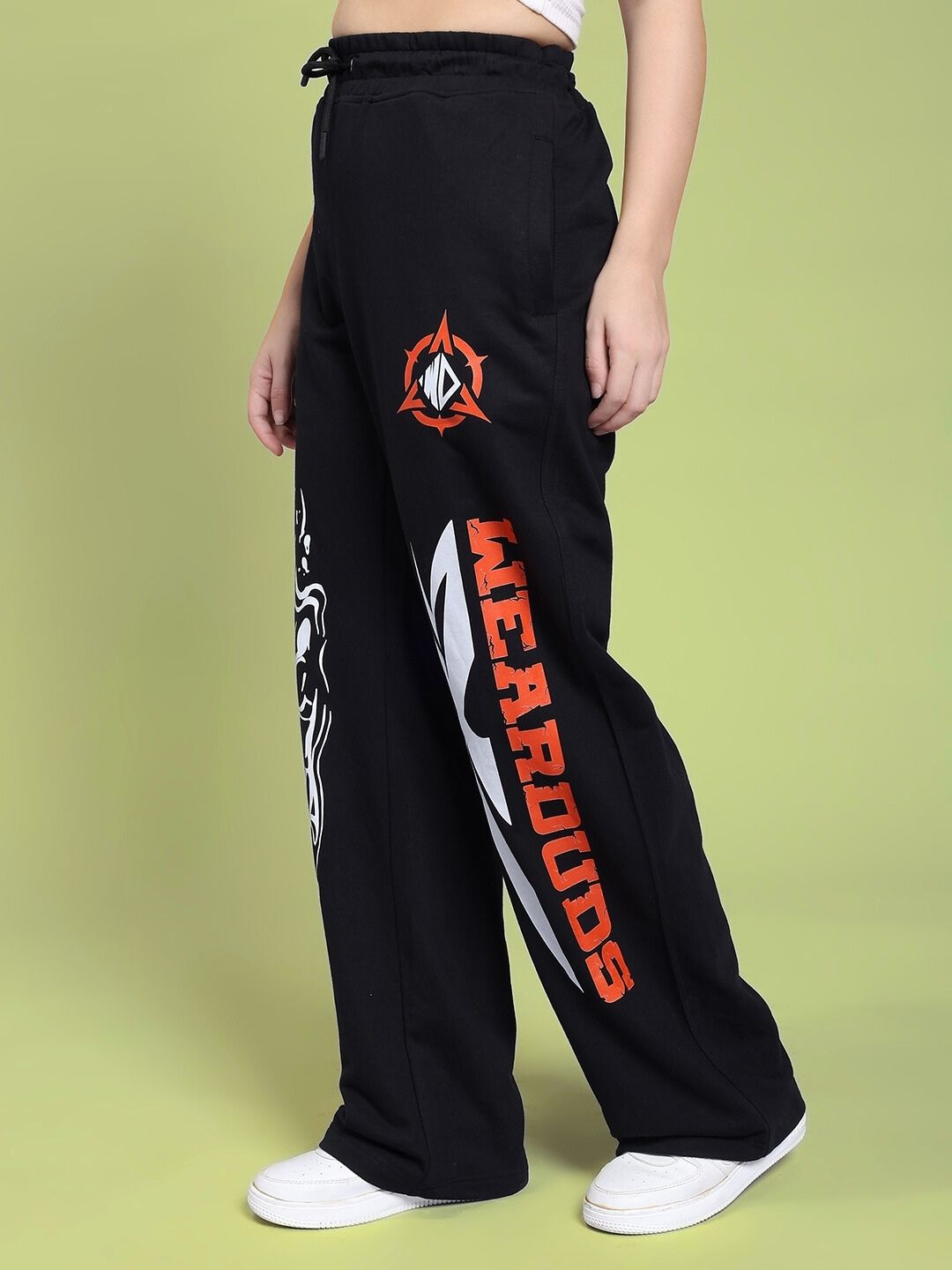 Side view of WOMEN RIFT RELAXED FIT JOGGER IN BLACK with graphic design, showcasing comfort and style on a green background.