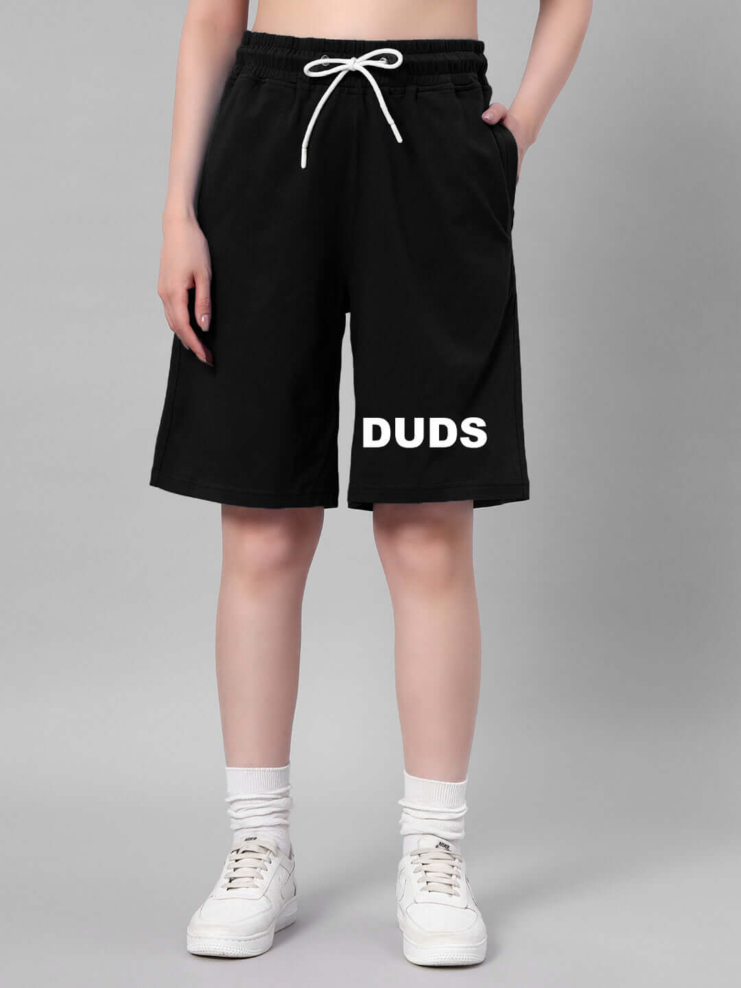 Person wearing black shorts with white drawstring and 'DUDS' text, styled with white sneakers and socks.