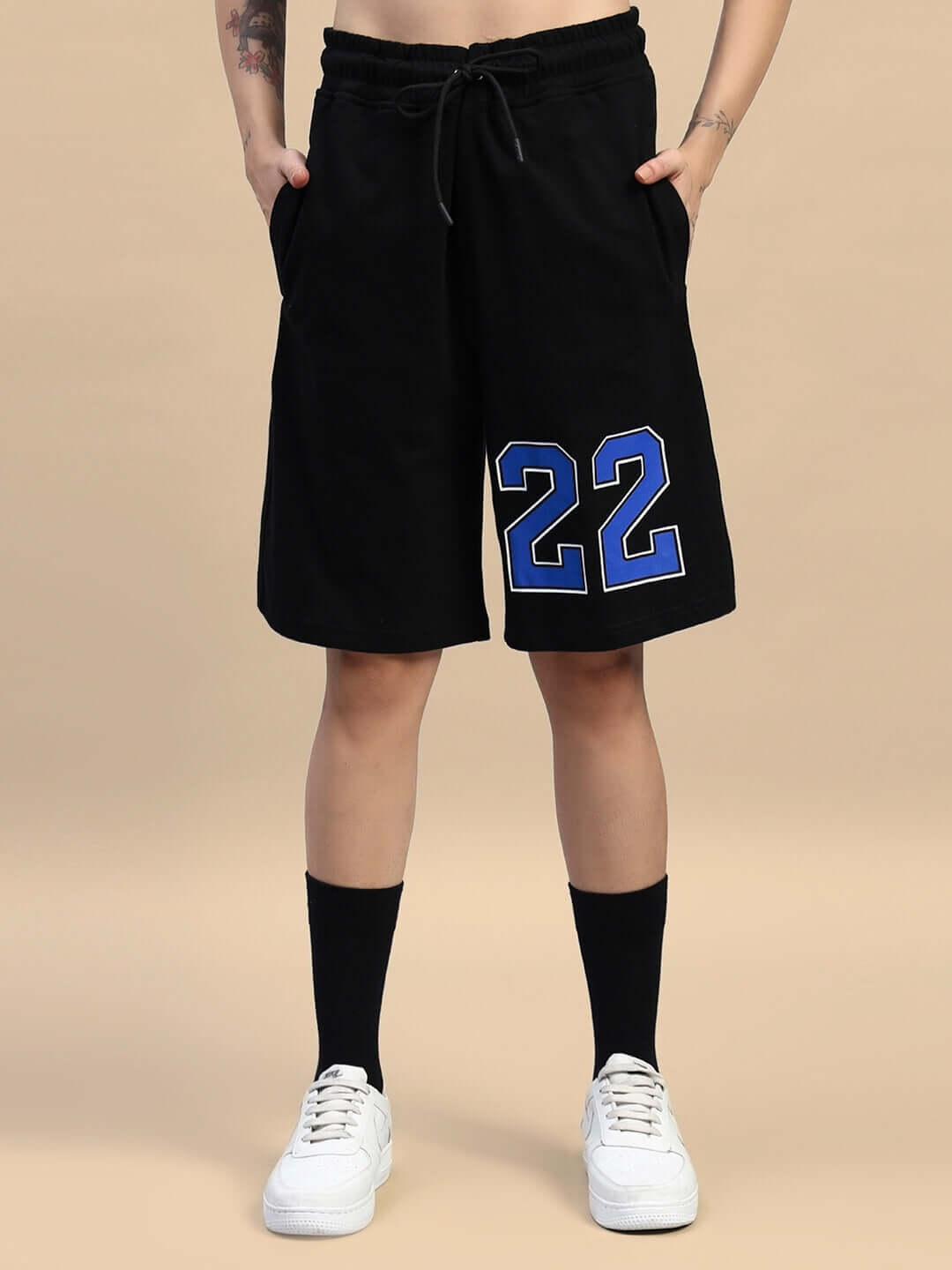 Person wearing black gym shorts with blue number 22, white sneakers, and black socks, standing on a neutral background.