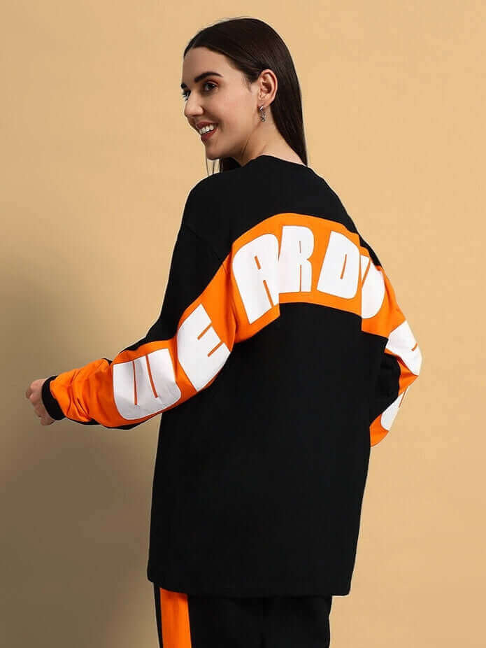 Model wearing WOMEN TITAN OVERSIZED SWEATSHIRT BLACK in a chic, casual style with contrasting orange sleeves.