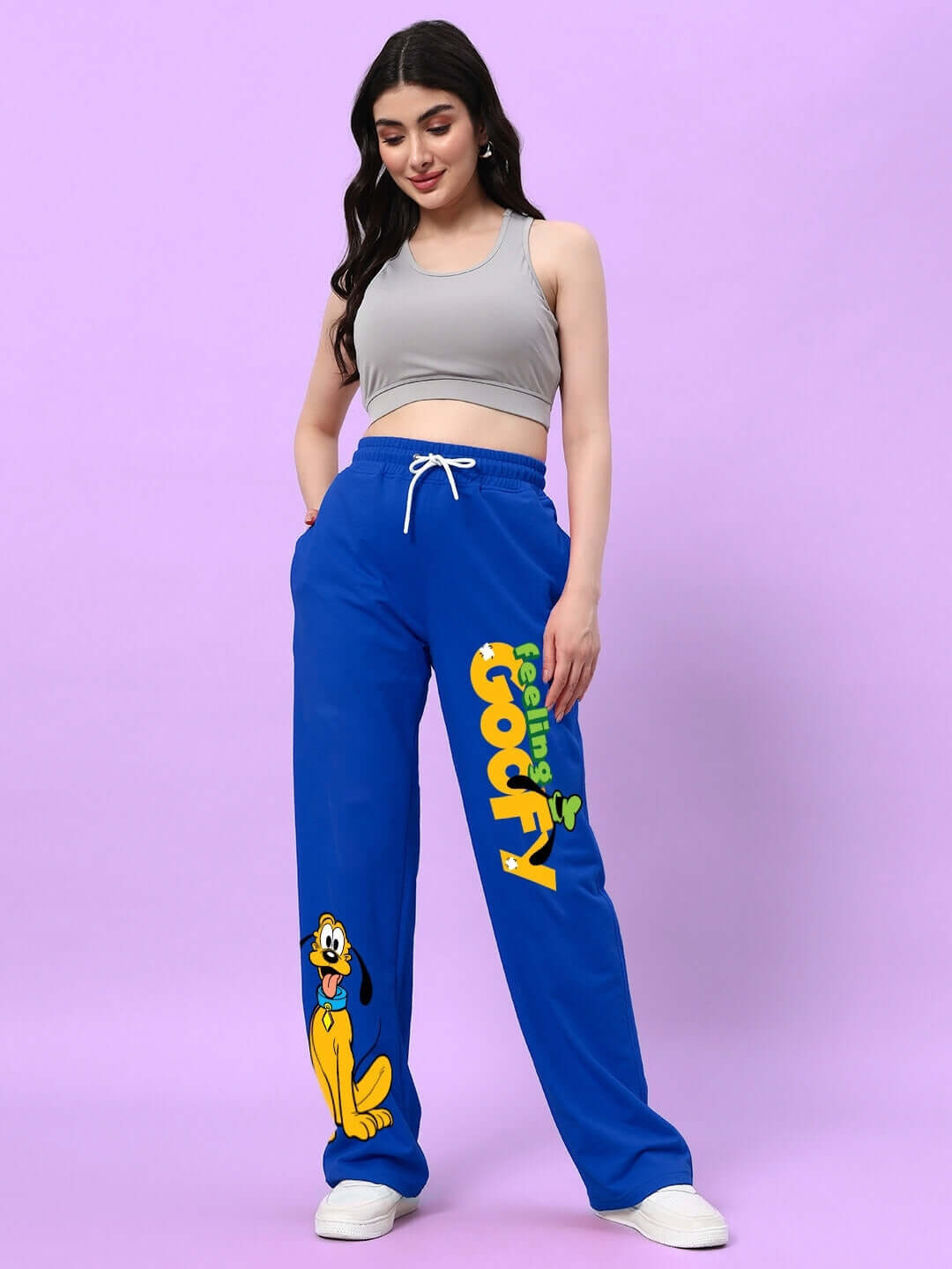 Woman wearing WOMEN'S FEELING GOOFY RELAXED FIT JOGGER BLUE with cartoon print, standing against a pink background.