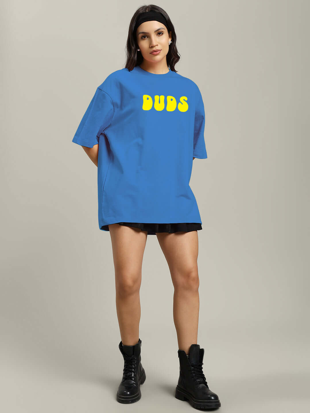 Woman wearing blue oversized t-shirt with 'DUDS' text, paired with black shorts and boots; made from premium cotton blend.
