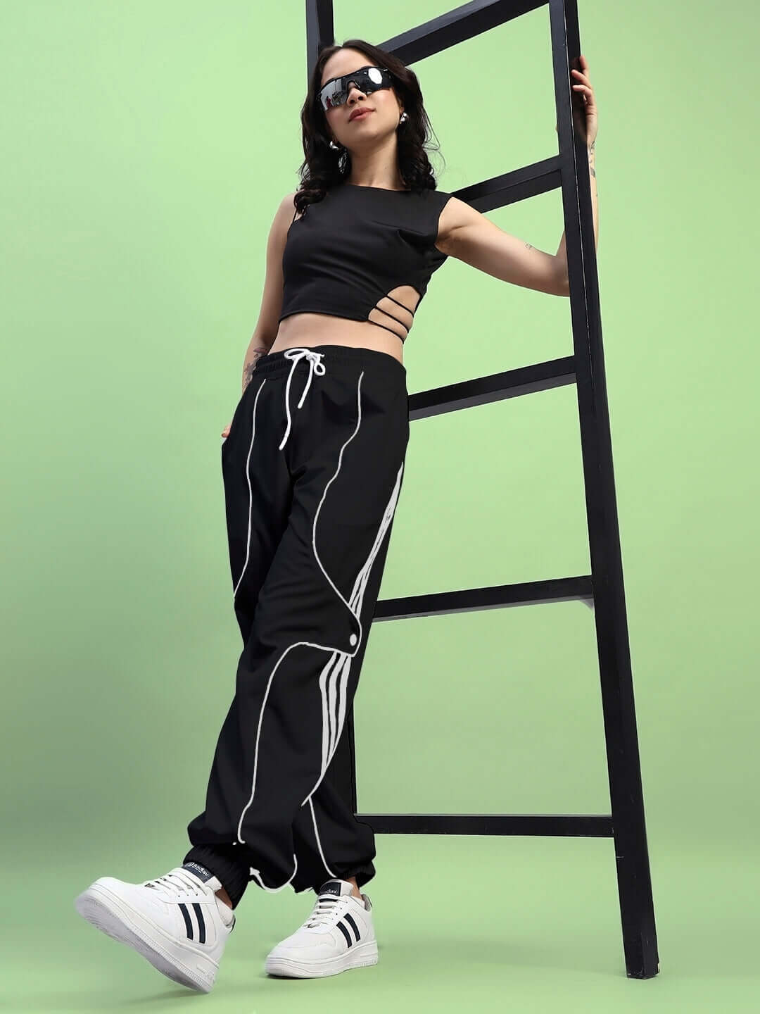 Woman in Womens Bolson Stripes Relaxed-Fit Joggers Black leaning against a ladder, showcasing stylish streetwear with white sneakers.
