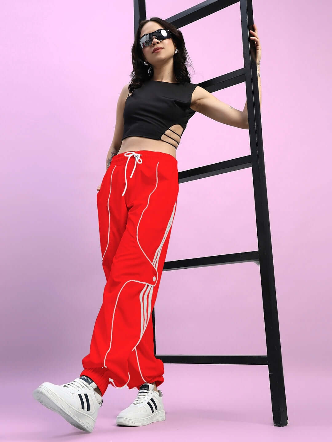 Model wearing women's red Bolson Stripes relaxed-fit joggers, paired with a black top and sneakers, leaning against a black ladder.