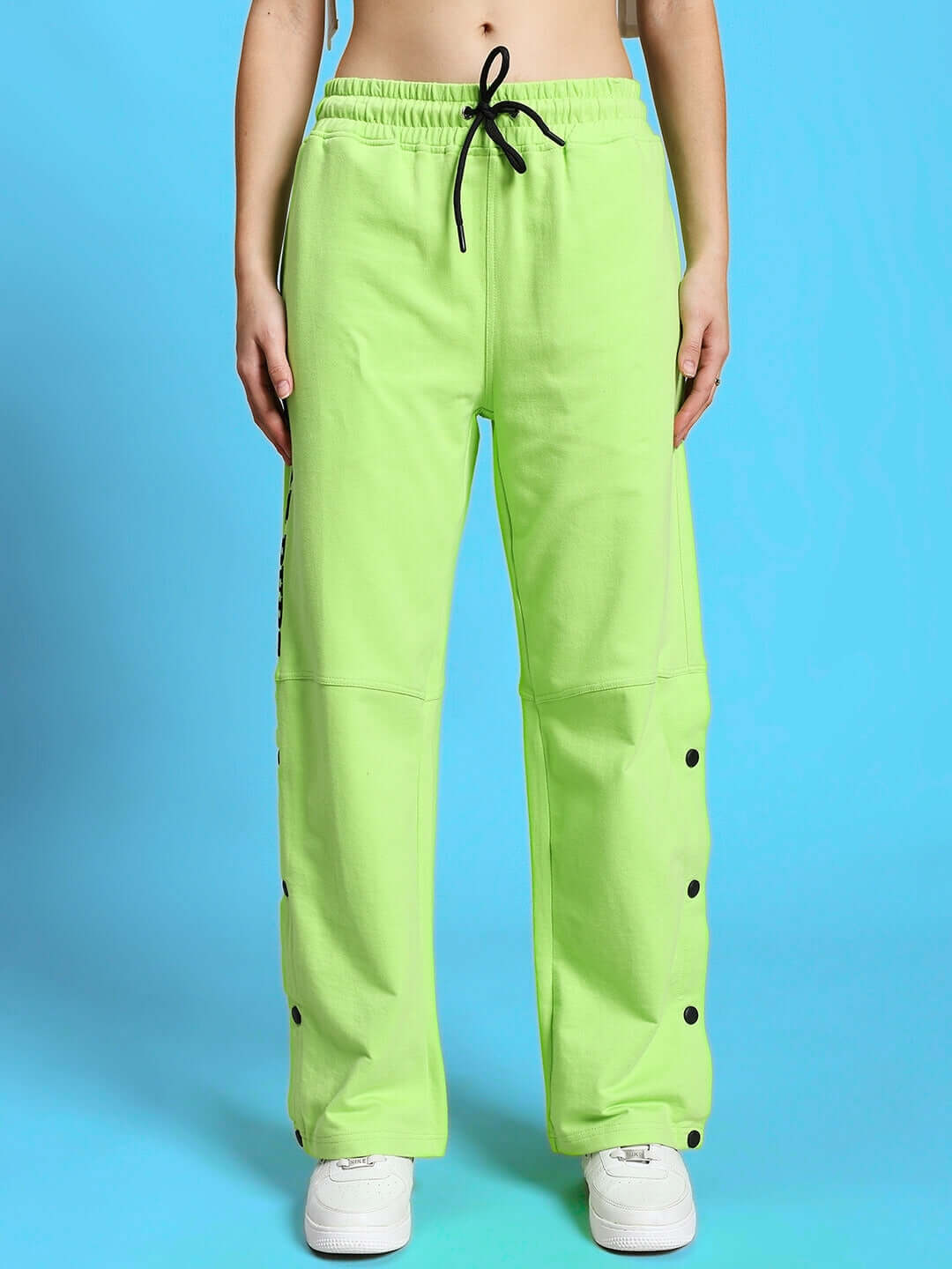 Model wearing WOMEN'S BROOKE CO-ORD SET NEON GREEN with stylish pants and drawstring detail on blue backdrop