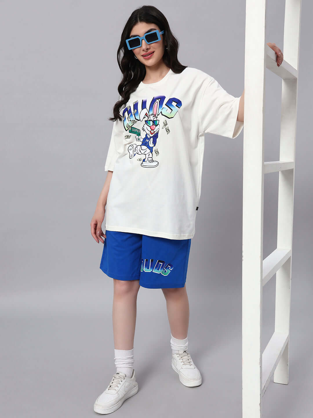 Woman wearing off-white and blue co-ord set with Bugs Bunny print, made from cotton French terry lycra, standing with sunglasses and sneakers.