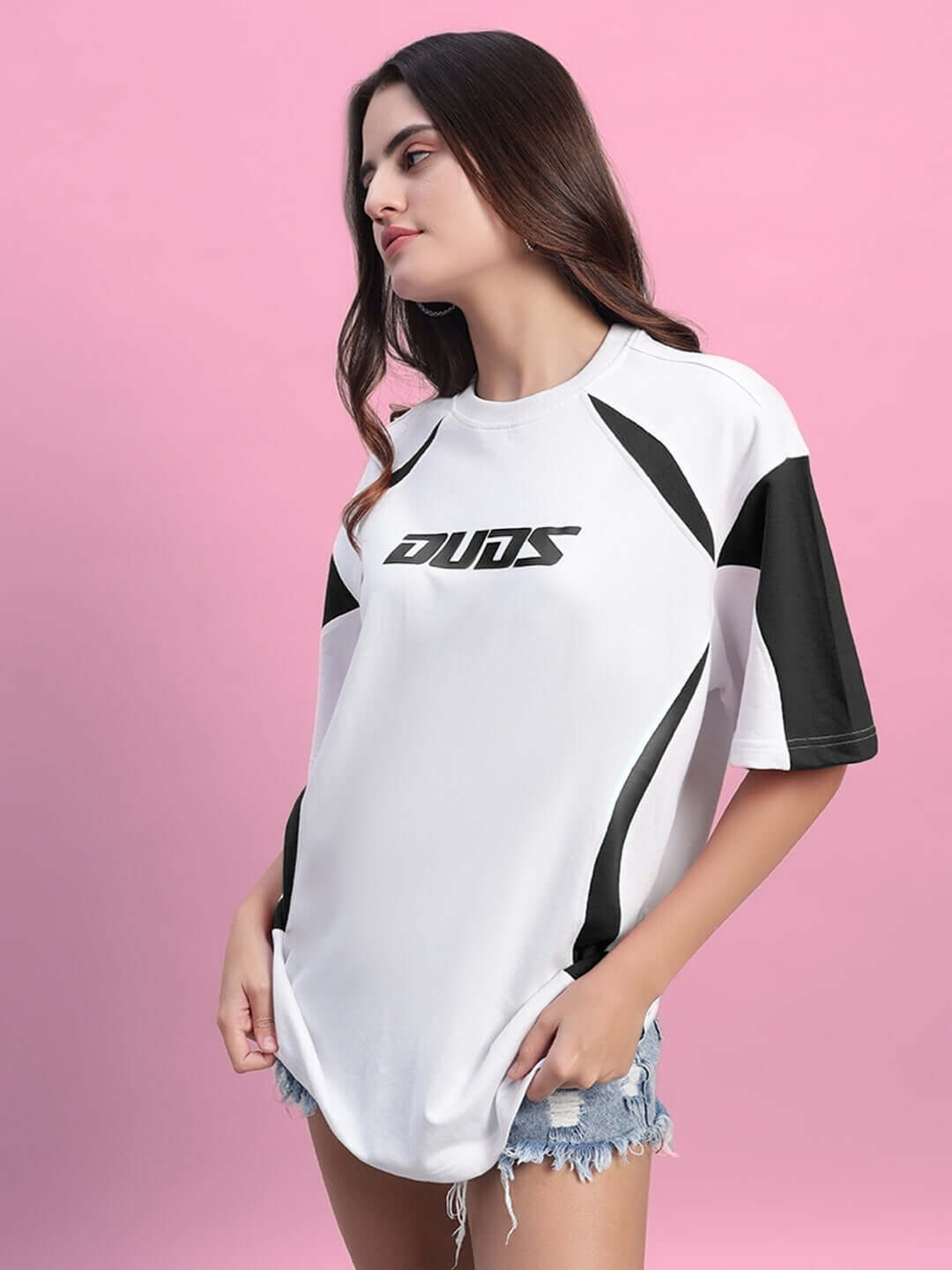 Woman wearing Women's Candor Over-sized T-shirt in white and black, made with premium heavy gauge fabric, styled casual on pink background.