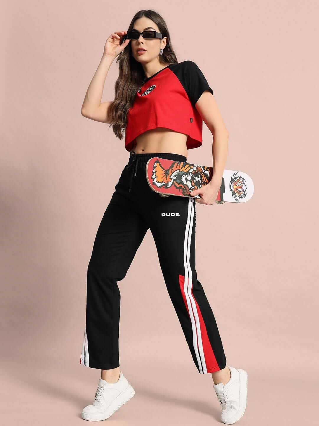 Woman wearing red and black raglan crop top, holding a skateboard, in sporty casual outfit.