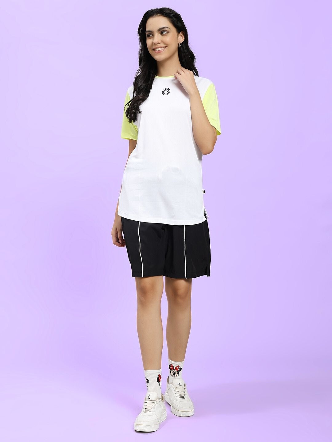 Woman wearing WOMEN CHAMPION ZONE FRONT PLATED SHORTS BLACK styled for casual streetwear look on a purple background.