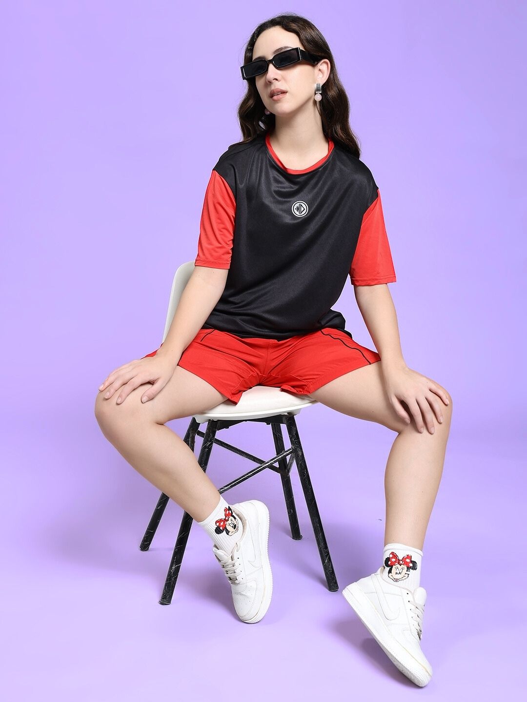 Woman wearing WOMEN'S CHAMPION ZONE FRONT PLATED SHORTS RED, sitting on a chair against a purple background.
