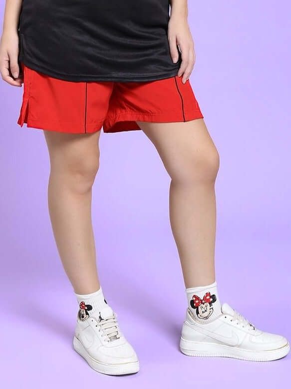 Woman wearing WOMEN CHAMPION ZONE FRONT PLATED SHORTS RED with sneakers, showcasing sporty streetwear style.