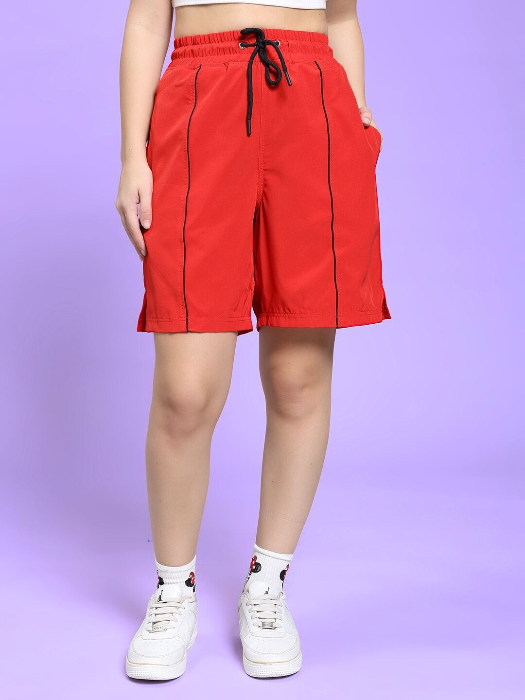 Model wearing WOMEN CHAMPION ZONE REGULAR FIT CO-ORD SET BLACK RED shorts with white sneakers on a purple background.