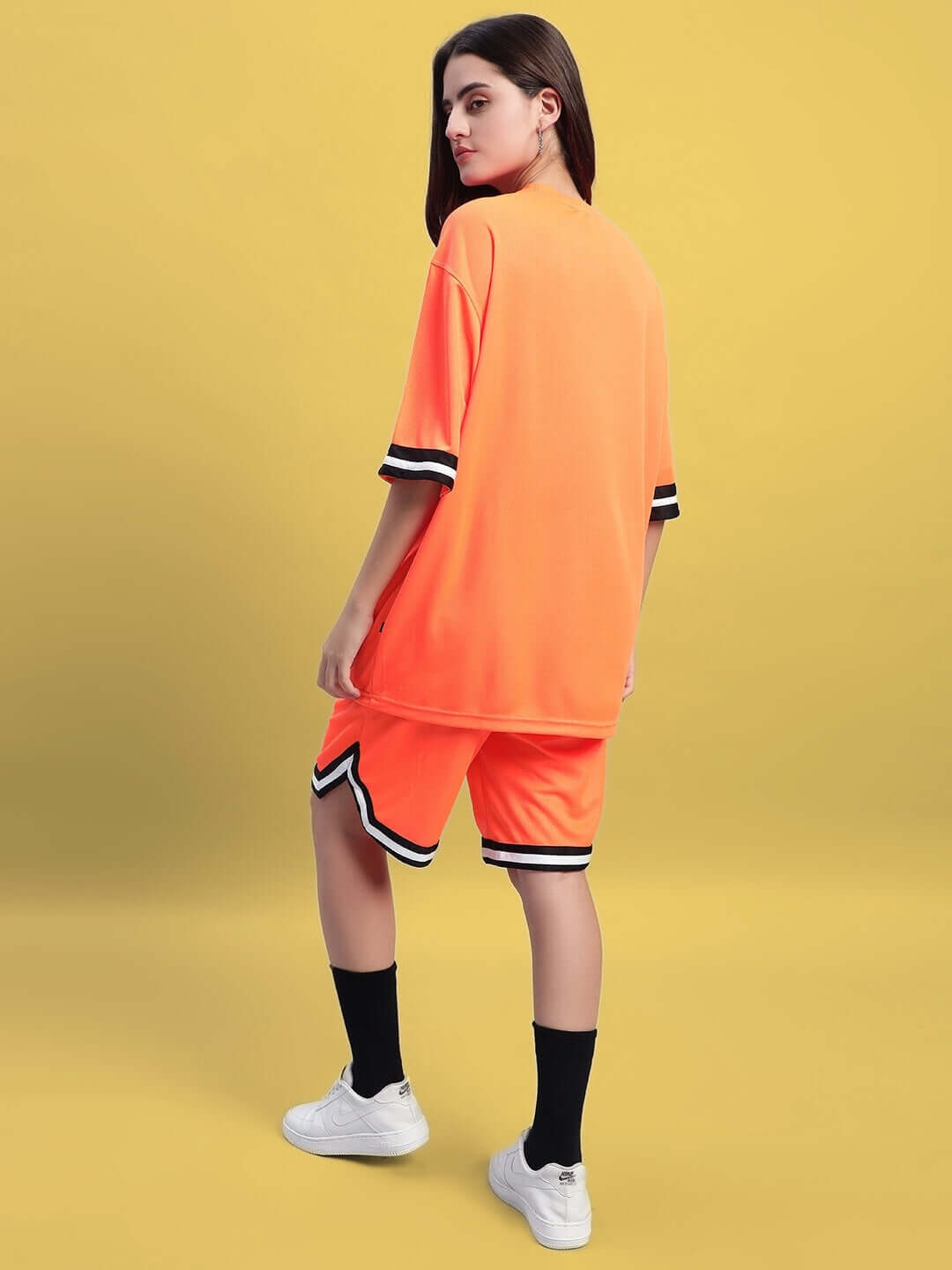Model wearing WOMEN'S CHRONIC COLORBLOCK CO-ORD SET ORANGE with vibrant orange accents, showcasing fashion-forward style on a yellow background.
