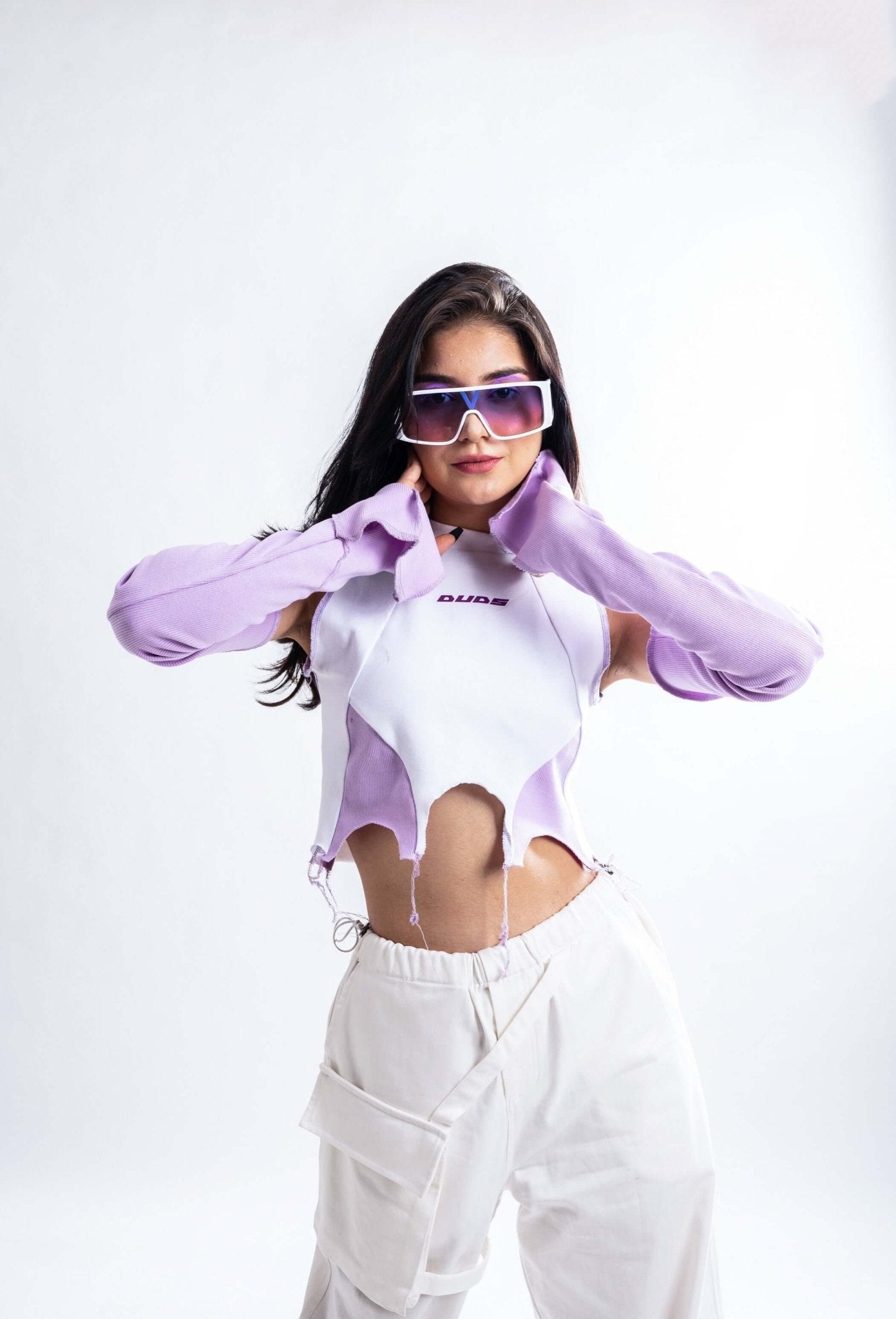 Stylish woman wearing WOMENS COLOR BLOCK CROP TOP WITH LONG SLEEVE, purple and white, with trendy sunglasses and high-waisted pants.