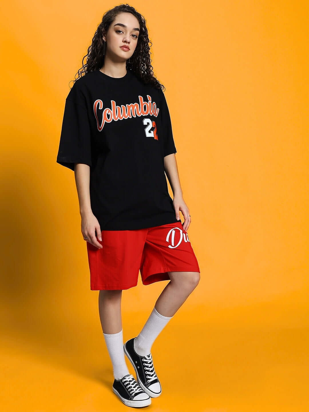Woman wearing WOMEN'S COLUMBIA 22 PRINT SUMMER CO-ORD SET BLACK RED with black top and red shorts, standing on a yellow background.
