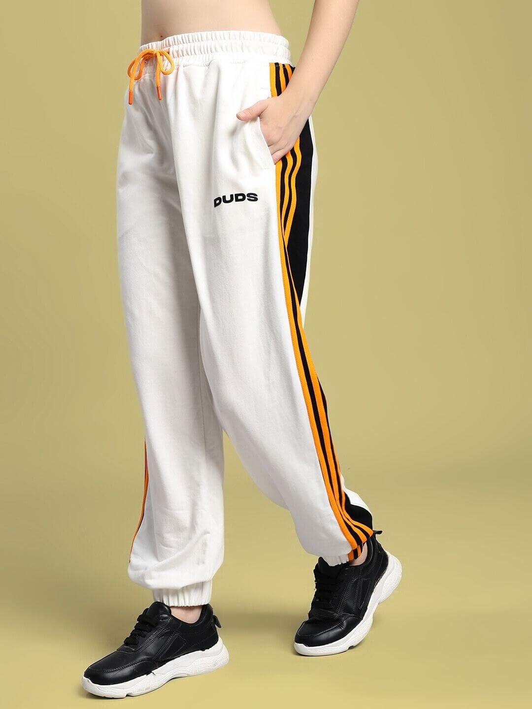 Woman wearing WOMEN'S COMFORT FLEX STRIPE JOGGER OFF-WHITE with black sneakers, off-white joggers featuring orange and black stripes.