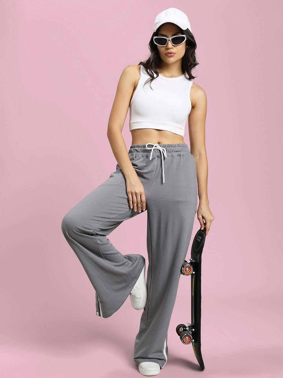 Model wearing women's grey contrast panel joggers with white top, holding a skateboard against a pink background.