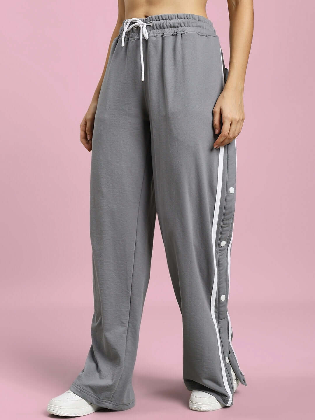 Women's grey contrast panel joggers with side buttons and an elastic waistband, showcased against a soft pink background.