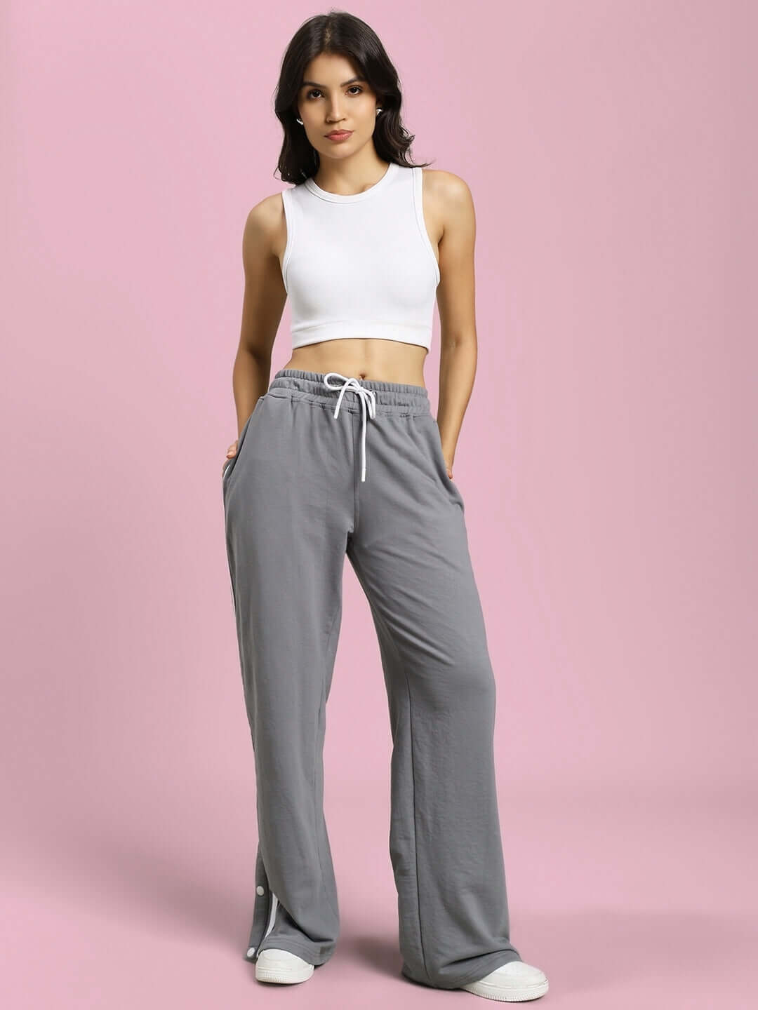 Woman in grey contrast panel jogger pants with white drawstring and white tank top, standing against a pink background.