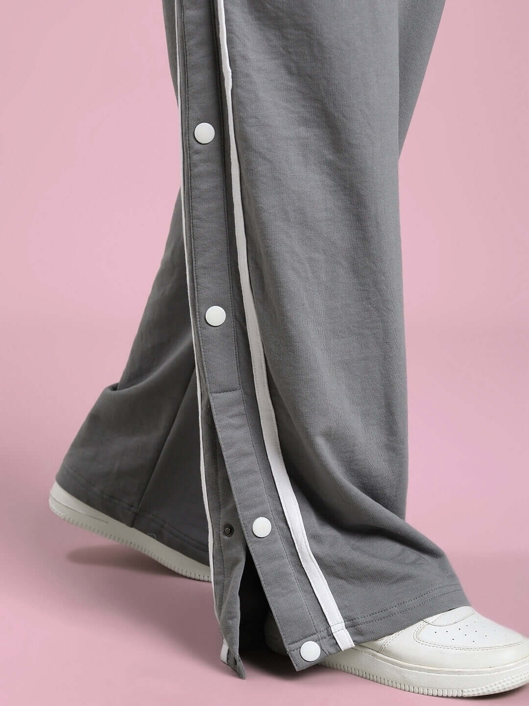 Close-up of grey women's contrast panel jogger showcasing button detailing and white sneakers against a pink background.