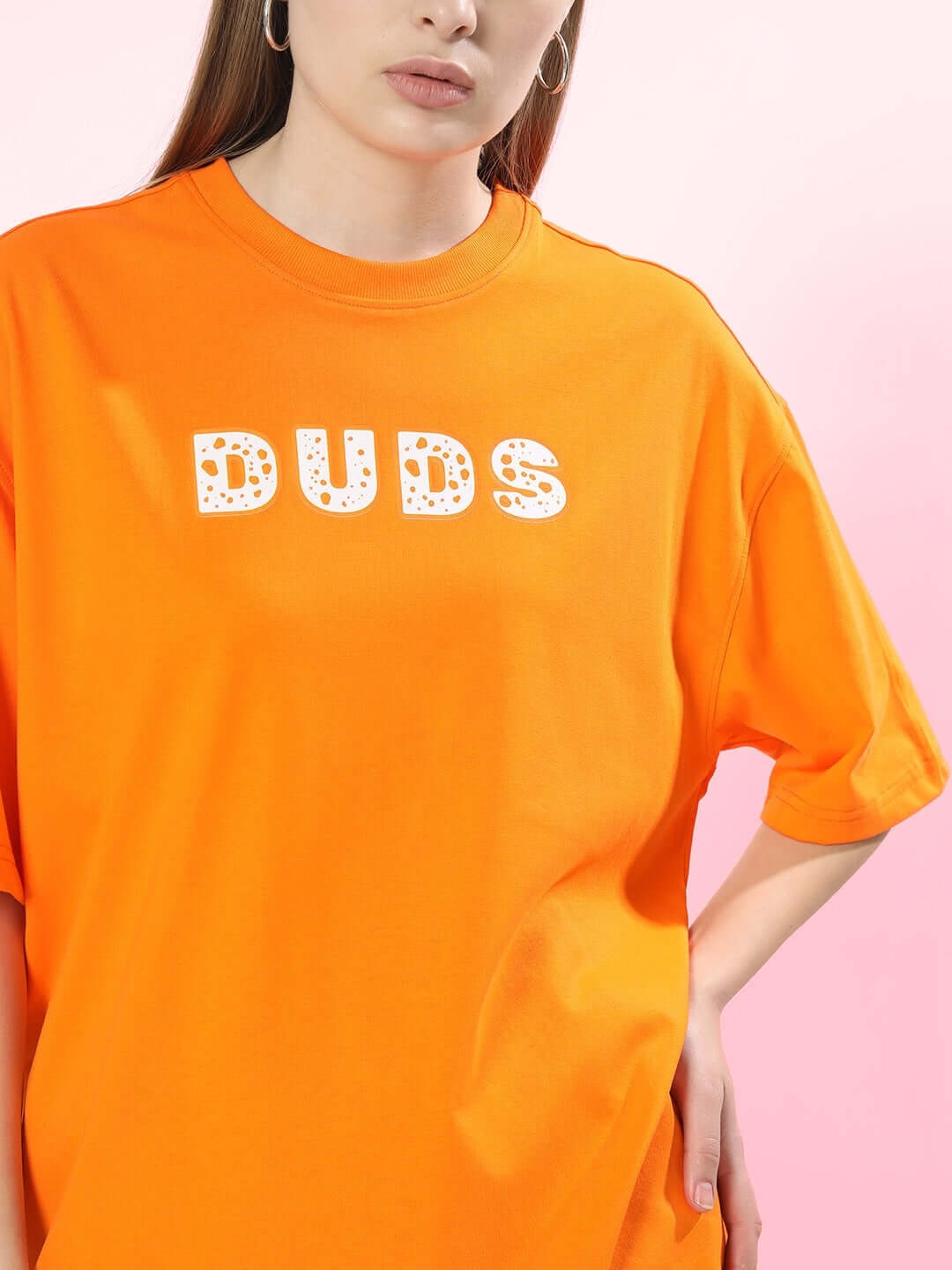 Woman wearing WOMEN COURAGE OVER-SIZED T-SHIRT ORANGE with "DUDS" graphic, showcasing bold statement fashion and comfort.