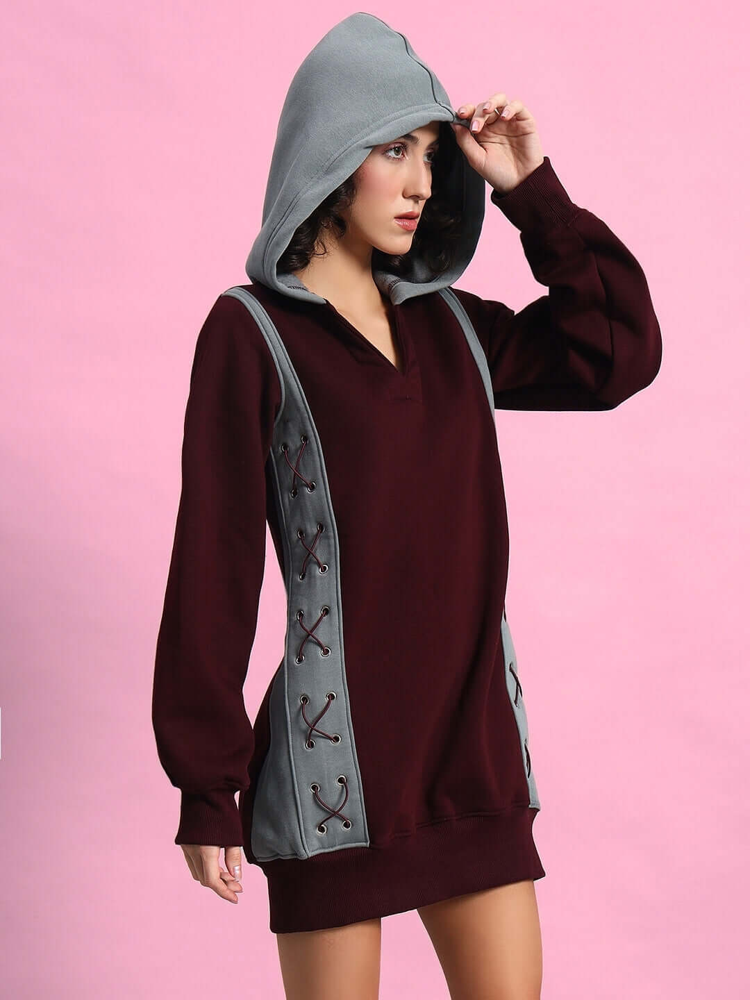 Woman wearing WOMEN CRISS CROSS FLEECE HOODIE WINE GREY with hood up against a pink background.
