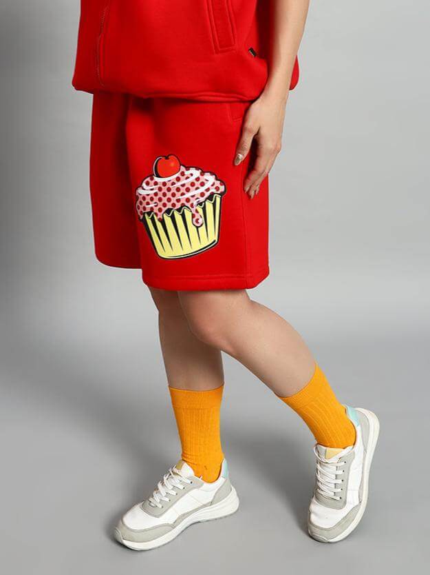 Model wearing WOMEN CUPCAKE FLEECE SHORTS RED with cupcake print, showcasing vibrant streetwear fashion and cozy fleece fabric.