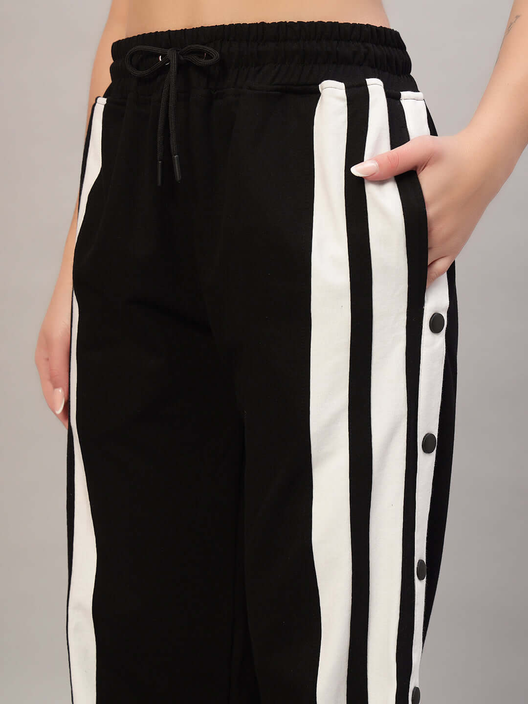Close-up of women's black and white joggers with side stripes and buttons, featuring a comfortable elastic waistband.