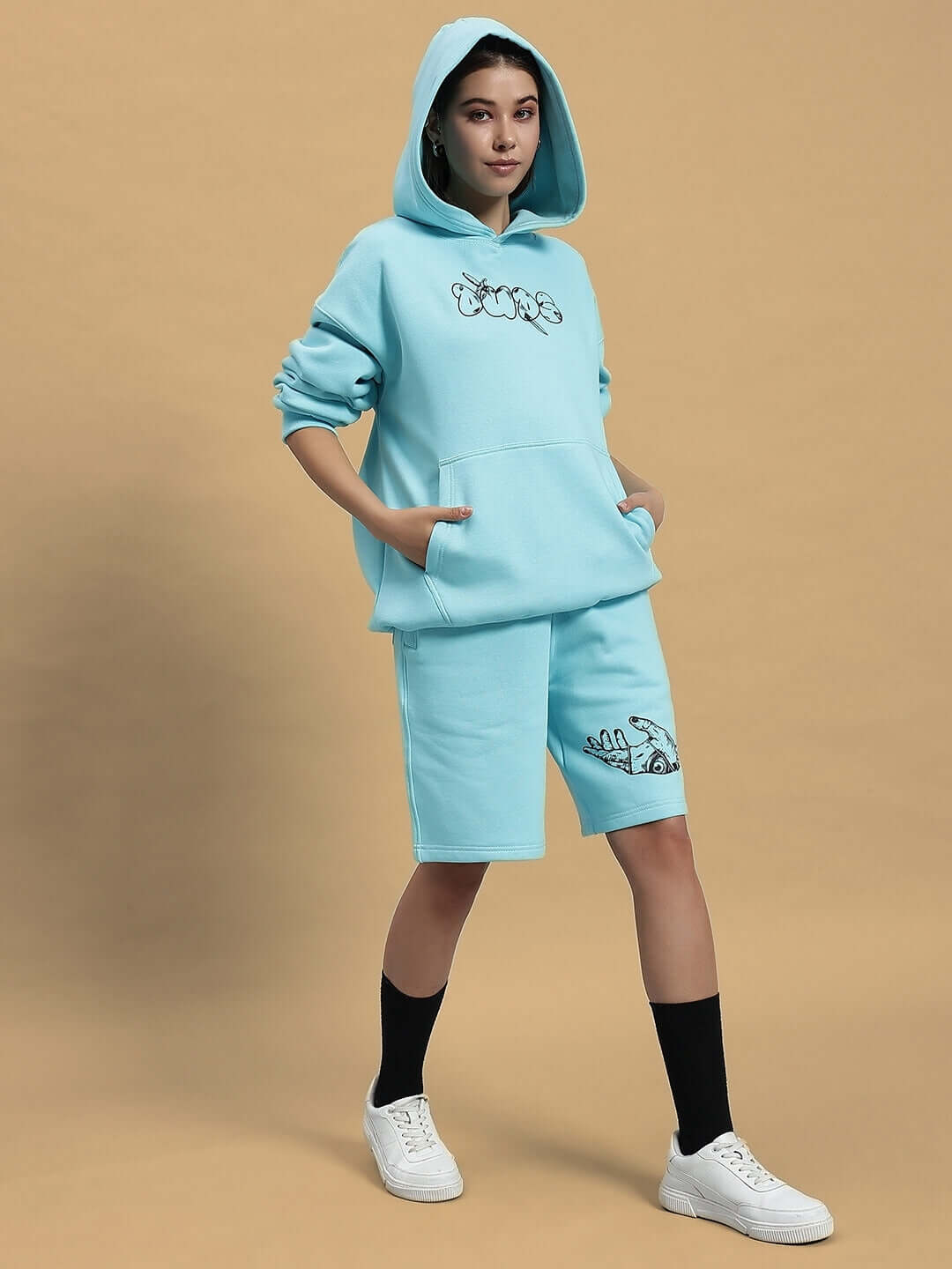 Woman wearing a WOMEN DEMON FLEECE CO-ORD SKY BLUE outfit, featuring a hoodie and shorts, standing against a beige background.