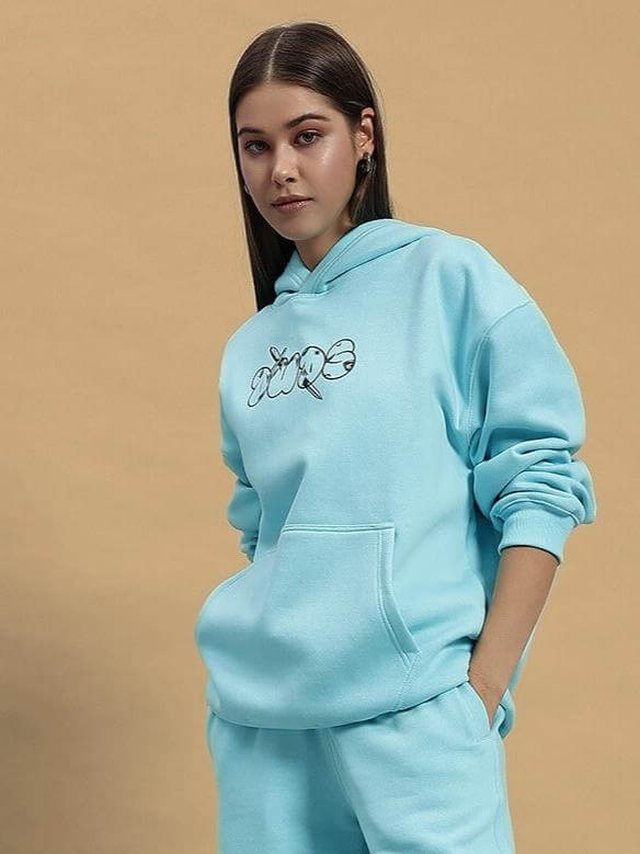 Woman wearing WOMEN DEMON FLEECE HOODIE SKY BLUE standing against a beige background.