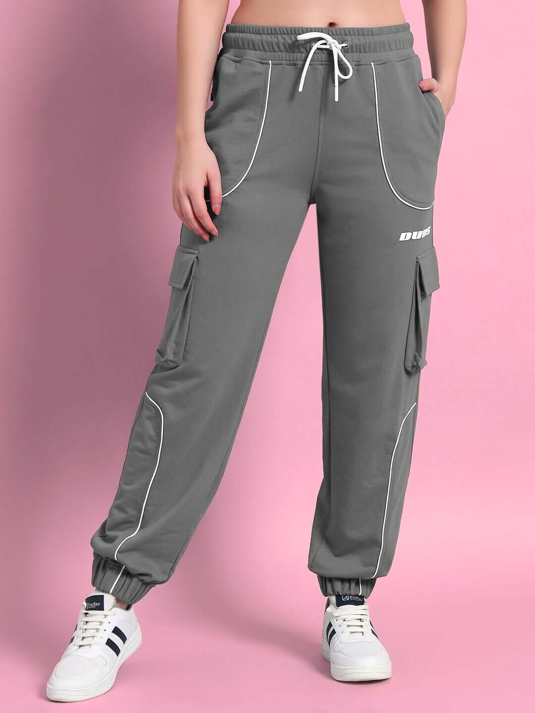 Women's grey relaxed-fit joggers by DUDS, featuring drawstring waist and side pockets, worn with white sneakers against a pink background.